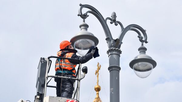 Сотрудник коммунальной службы протирает плафон фонаря наружного освещения на Пречистенской набережной в Москве