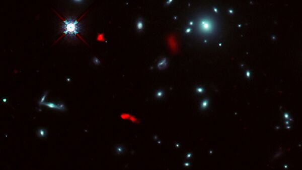 Фото скопления галактик RXCJ0600-2007, выполненное космическим телескопом Хаббл, с наложенным на него изображением галактики RXCJ0600-z6 (красным), полученное телескопом ALMA. Из-за эффекта гравитационного линзирования изображение галактики было усилено и оказалось разделенным на три части