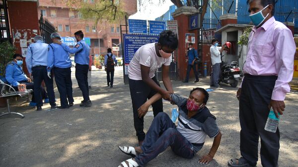 Мужчина помогает подняться упавшему у входа на территорию госпиталя в Дели