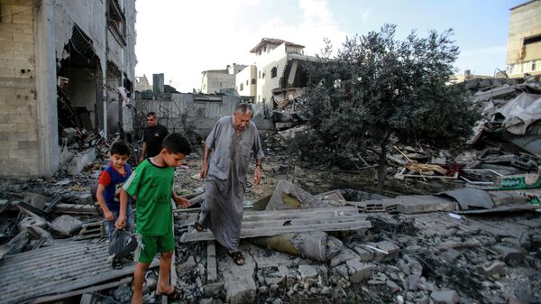 Местные жители ходят по завалам разрушенного в результате бомбардировки здания в секторе Газа