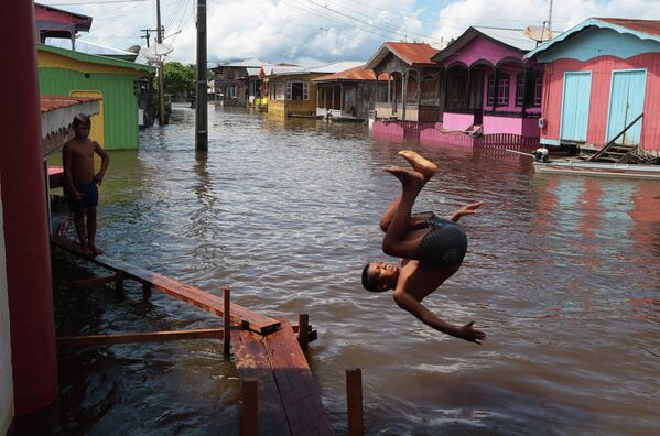 Мальчик прыгает в воду на затопленной улице в Анаме, штат Амазонас, Бразилия