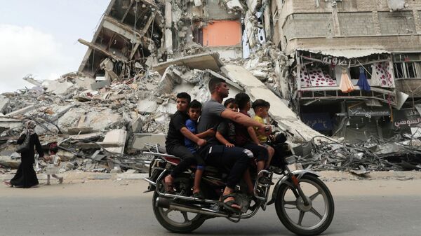 Палестинцы проезжают мимо здания, разрушенного в результате бомбардировки в секторе Газа, после объявления о прекращении огня между Израилем и ХАМАС