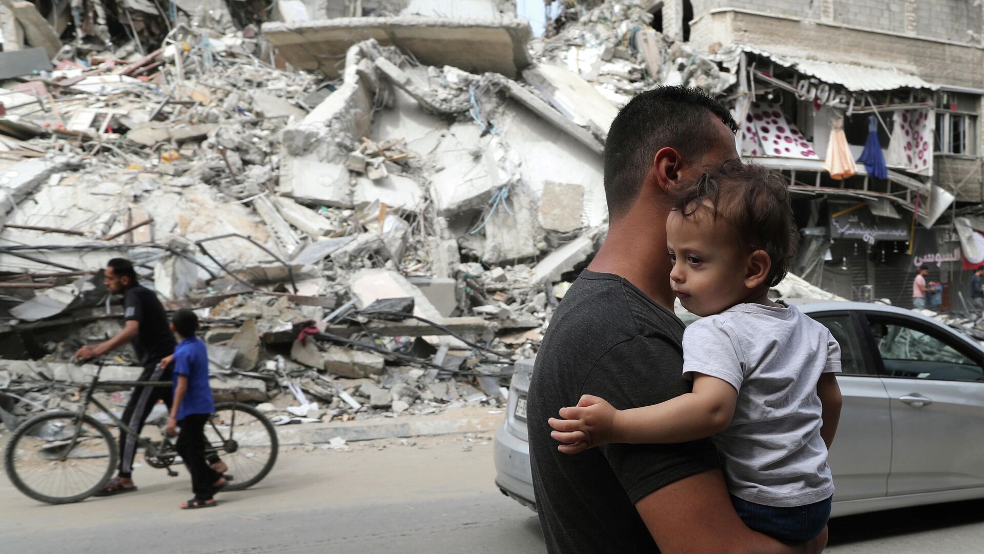 Палестинец с ребенком проходит мимо разрушенных в результате бомбардировки зданий в секторе Газа, после объявления о прекращении огня между Израилем и ХАМАС - РИА Новости, 1920, 01.06.2021
