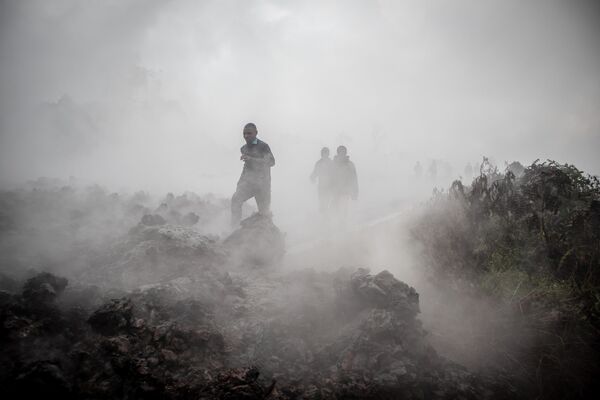 Мужчины идут мимо дымящейся лава после извержения вулкана Ньирагонго в Демократической республике Конго