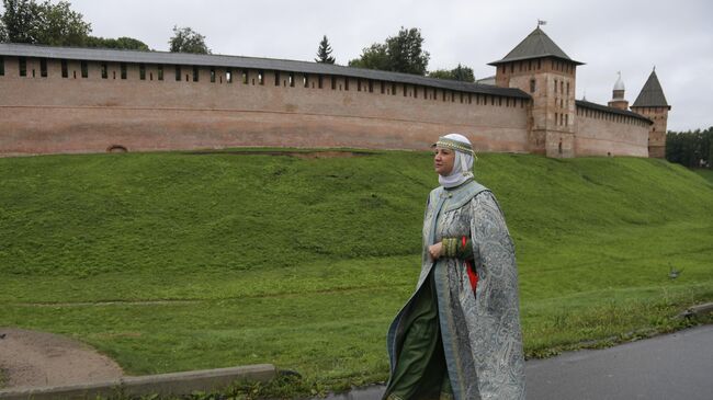 Экскурсовод в традиционной русской одежде на фоне Кремля в Великом Новгороде