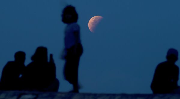 Жители наблюдают за лунным затмением на пляже Санур на Бали, Индонезия. 26 мая 2021