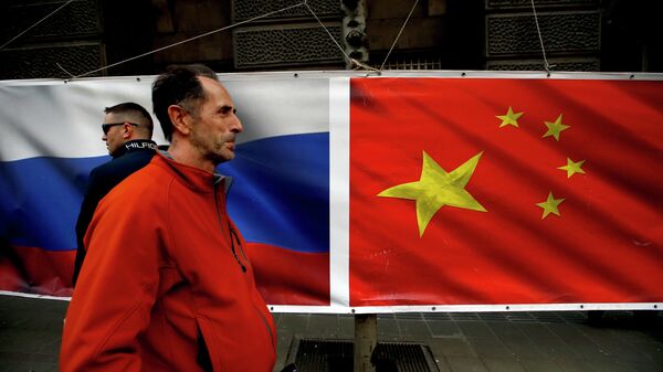 Люди проходят мимо баннера с флагами России и Китая