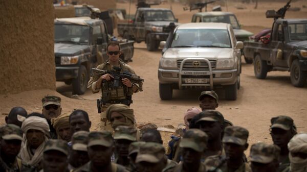 Французский солдат стоит позади малийских солдат во время операции Сервал