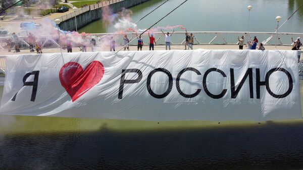 Участники акции в честь Дня России на Мосту Поцелуев в Краснодаре с баннером Я люблю Россию