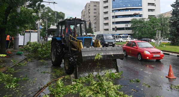Работник коммунальной службы на тракторе убирает поваленные ветви деревьев после сильного ливня в Ростове-на-Дону