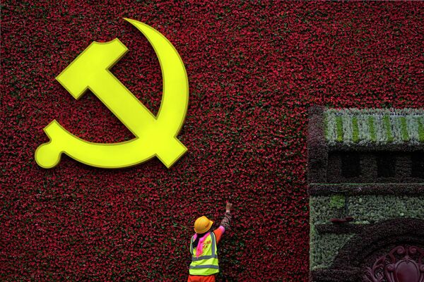 Рабочий устанавливает цветочное украшение в форме флага с символом Коммунистической партии в Пекине