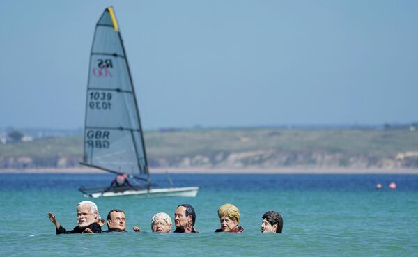 Протестующие с гигантскими головами, изображающими лидеров G7, плавают в воде во время демонстрации перед встречей G7 в Сент-Айвсе, Корнуолл, Англия