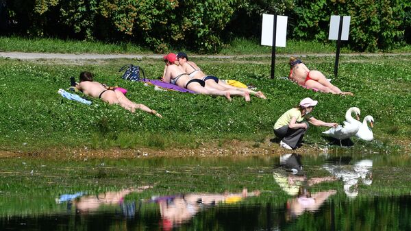 Люди загорают на газоне у пруда в жаркую погоду в парке культуры и отдыха Сокольники в Москве