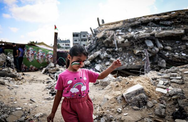 Палестинская девочка с нарисованным на лице национальным флагом играет среди обломков зданий, разрушенных в результате израильской бомбардировки сектора Газа в Бейт-Лахии