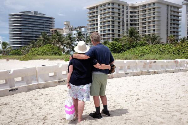 Пара на пляже смотрит частично обрушенное здание в городе Серфсайд под Майами, штат Флорида, США