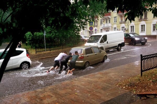 Молодые люди толкают автомобиль на одной из улиц в Москве во время дождя