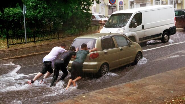 Молодые люди толкают автомобиль на одной из улиц в Москве во время дождя