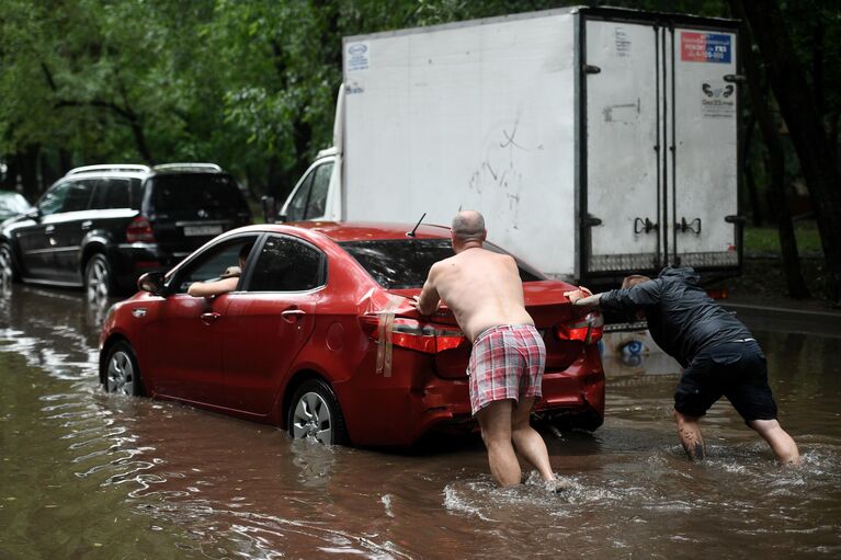Мужчины толкают автомобиль на одной из улиц в Москве во время дождя Мужчины толкают автомобиль на одной из улиц в Москве во время дождя