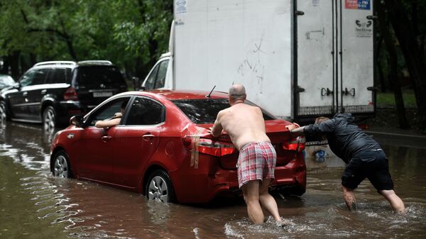 Мужчины толкают автомобиль на одной из улиц в Москве во время дождя