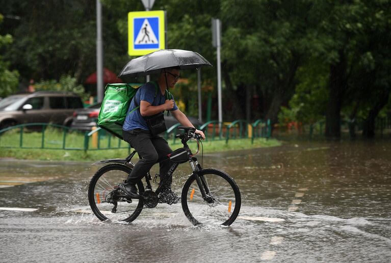 Мужчина едет на велосипеде по одной из улиц в Москве во время дождя Мужчина едет на велосипеде по одной из улиц в Москве во время дождя