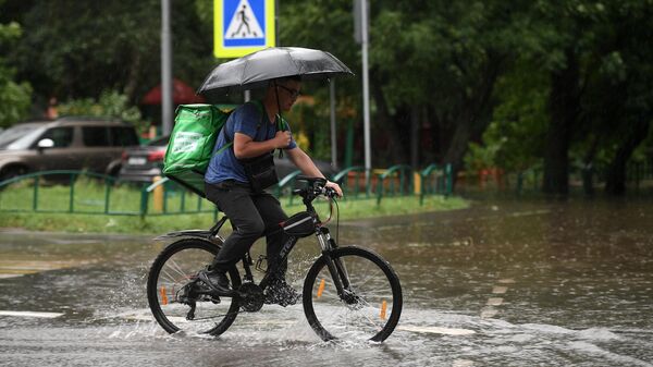 Мужчина едет на велосипеде по одной из улиц в Москве во время дождя