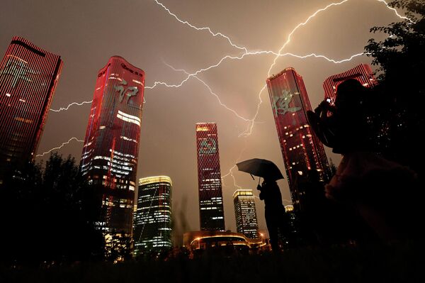 Молния пересекает небо, когда люди смотрят на здания, демонстрирующие световое шоу накануне 100-летия коммунистической партии Китая в Пекине