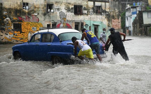 Мужчины толкают старую американскую машину на затопленной улице в Гаване, Куба