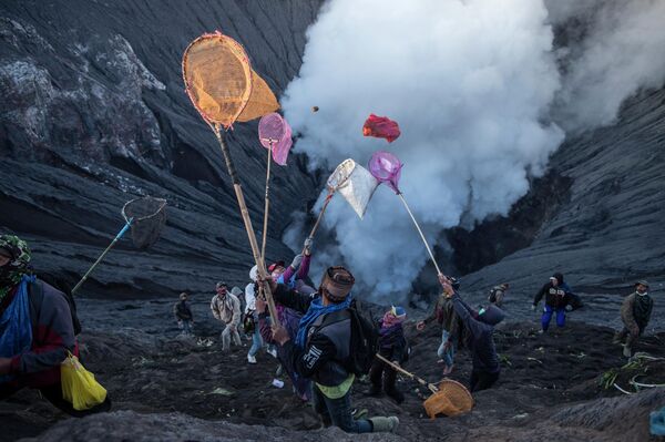 Люди пытаются поймать подношения, брошенные представителями племени Тенггер с вершины действующего вулкана Бромо в Проболингго, провинция Восточная Ява