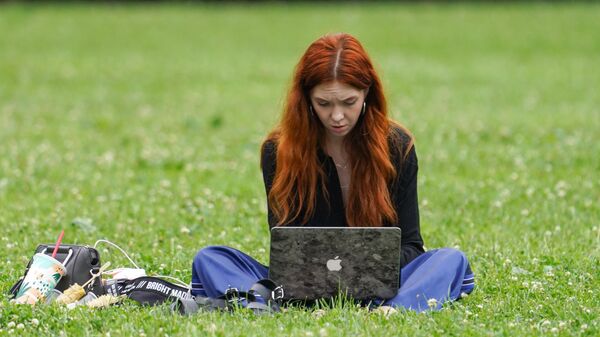 Девушка с ноутбуком сидит на траве