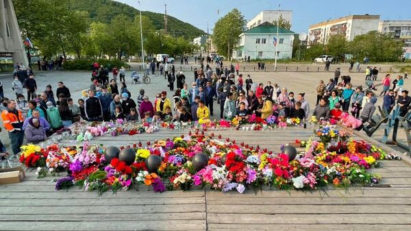 Люди несут цветы, свечи и портреты в память о погибших в авиакатастрофе к стихийному мемориалу на площади Ленина в поселке Палана