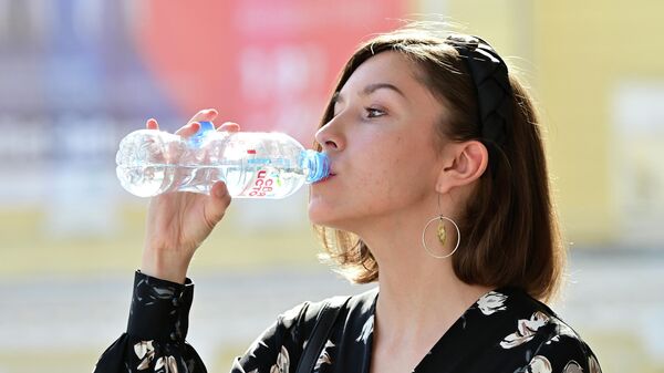 Девушка пьет воду во время жаркой погоды