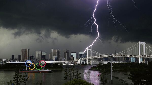 Молния видна над гигантскими олимпийскими кольцами и Радужным мостом, в Токио, Япония