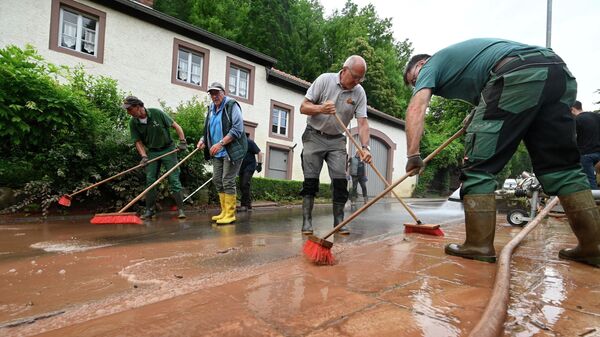 Жители очищают улицу от грязи после наводнения. Бирсдорф-ам-Зее, недалеко от Битбурга, Западная Германия