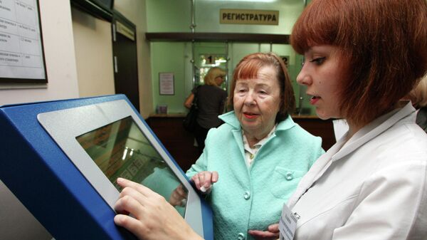 Сотрудница регистратуры и пожилая женщина у терминала электронной записи