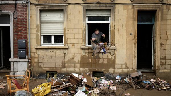 Жилец дома выбрасывает поврежденные предметы из окна после наводнения в Энсивале, Бельгия