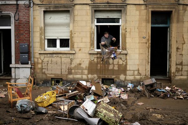 Жилец дома выбрасывает поврежденные предметы из окна после наводнения в Энсивале, Бельгия