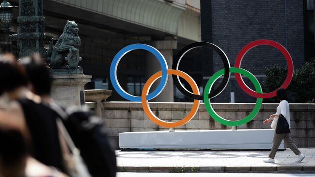 Женщина идет мимо олимпийских колец в Токио