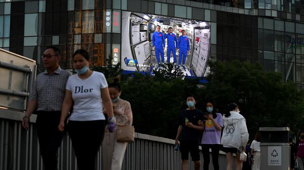 Люди проходят мимо экрана с репортажем о китайских астронавтах во время их первой миссии на китайской космической станции
