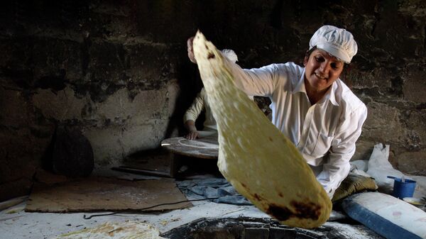 Женщина вынимает готовый лаваш из тандыра 