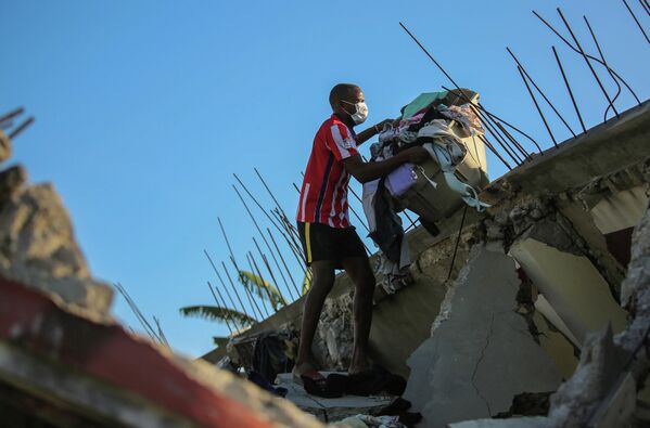 Мужчина собирает вещи из своего дома, разрушенного землетрясением в Ле-Ке, Гаити