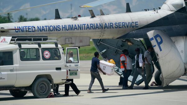 Люди загружают предметы первой необходимости из машины скорой помощи Врачей без границ в вертолет Организации Объединенных Наций, направляющийся к разрушенному землетрясением город Ле-Ке, Гаити