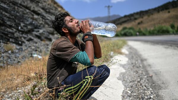 Афганский мигрант пьет воду, отдыхая на обочине дороги, Татван, Турция