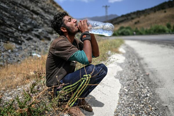 Афганский мигрант пьет воду, отдыхая на обочине дороги, Татван, Турция