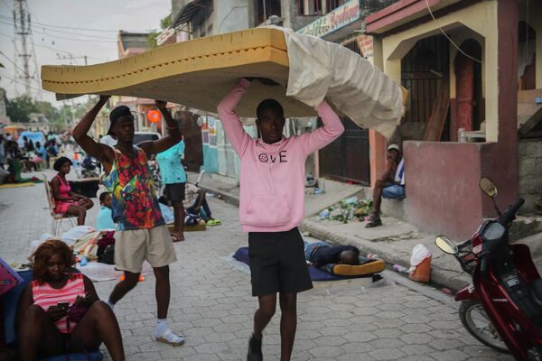 Мужчины несут матрас, пока люди спят на улице после землетрясения в Ле-Ке, Гаити