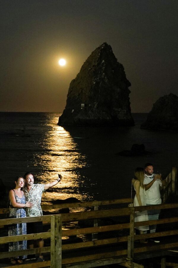 Люди фотографируются на фоне полной луны в Катании, Италия