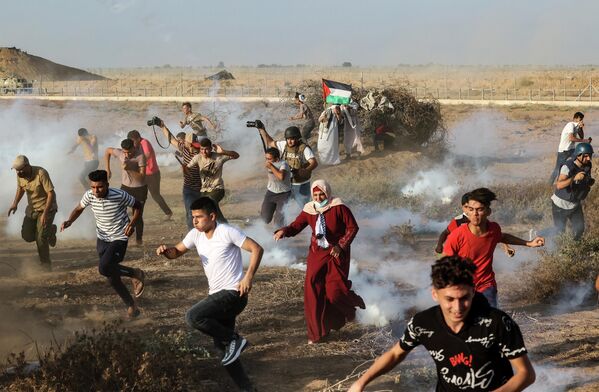 Палестинские демонстранты и журналисты бегут от слезоточивого газа, примененного израильскими силами безопасности во время акции протеста на юге сектора Газа