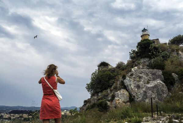 Девушка фотографирует маяк на вершине Старой крепости города Керкиры на греческом острове Корфу