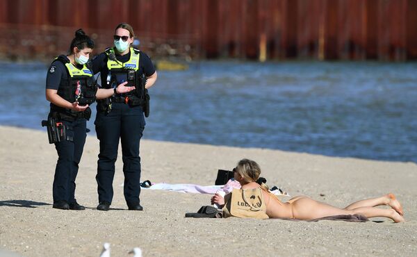 Сотрудники полиции разговаривают с девушкой, отдыхающей на пляже в Мельбурне, Австралия 