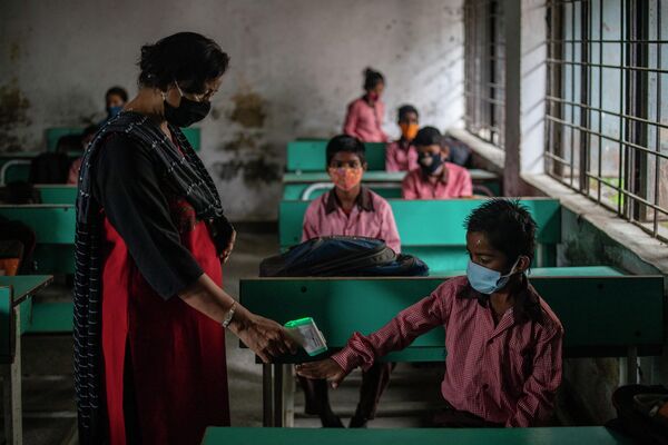 Учитель проверяет температуру тела ученика в первый день частичного открытия школ в Ноиде, пригороде Нью-Дели, Индия