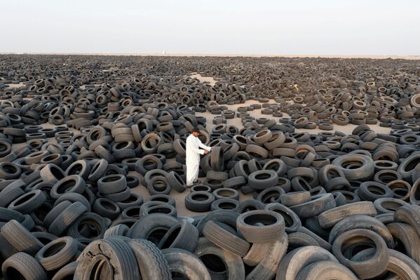 Рабочий стоит среди автомобильных шин, предназначенных для переработки в Кувейте